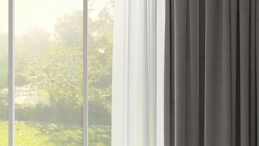 Bay window with beige-toned patterned valance and curtains, horizontal blinds, and a dining table with a chair.