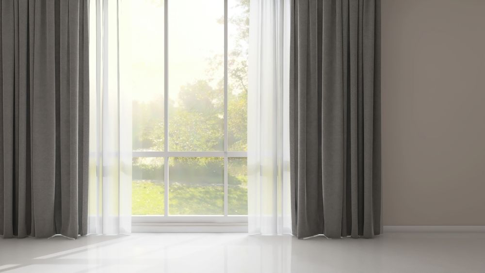 Gray room with three windows, gray curtains, mirror, and cleaning supplies on the floor.