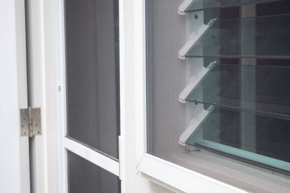 Exterior doorway with a screen door slightly ajar, set in a brick wall.
