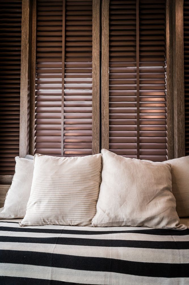Cozy seating area with white pillows on striped cushion; wooden shutter background.