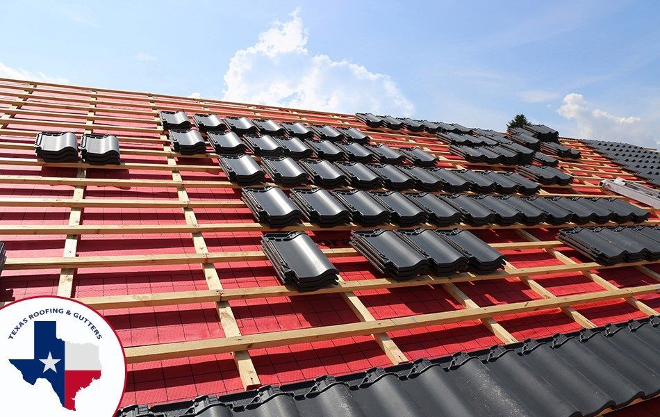 Roof under construction with black tiles and wood beams against a blue sky