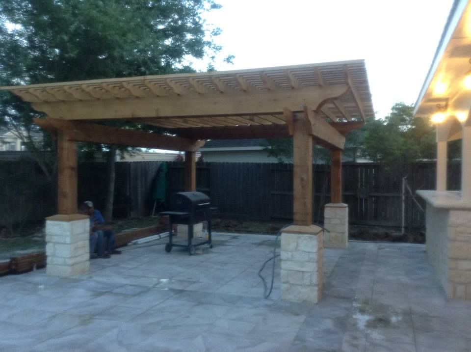 Patio with wooden pergola and stone columns, barbecue grill, and concrete flooring.