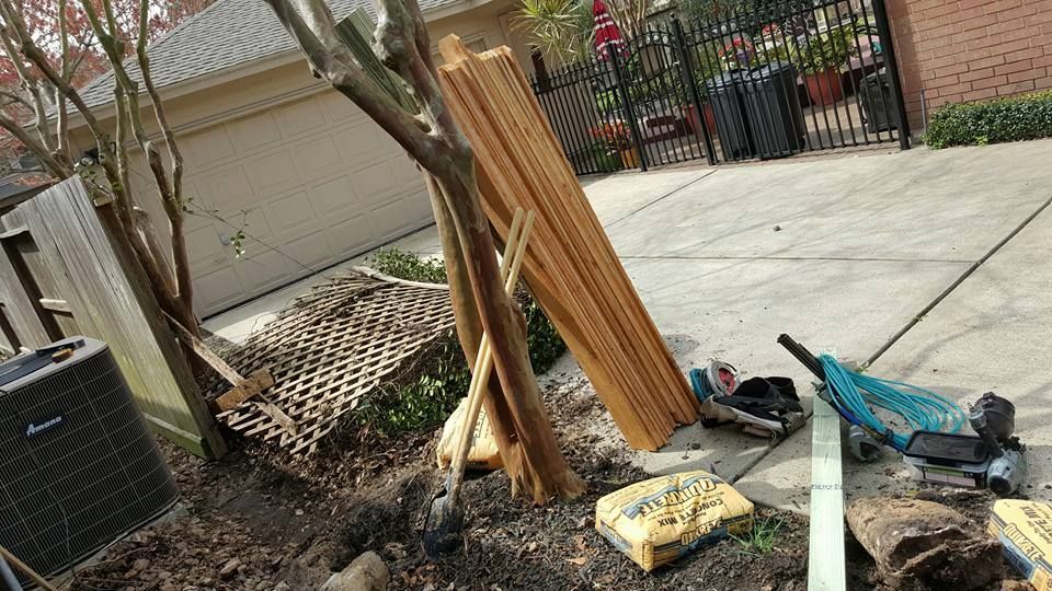 Construction site with lumber, tools, and a tree next to a driveway and garage.