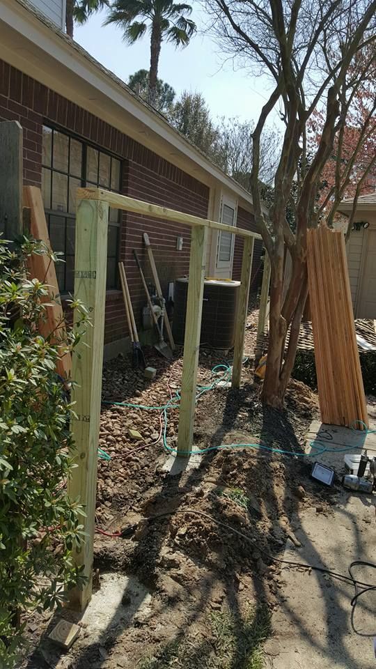 Fence under construction next to a brick building and a tree. Lumber and tools are visible.