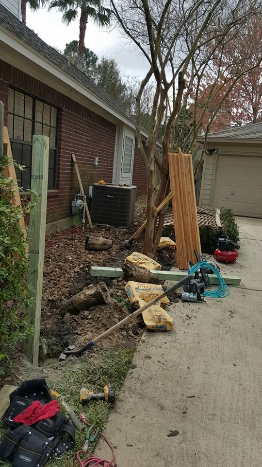 Construction site. Fence posts, wood, tools next to a brick house and driveway.