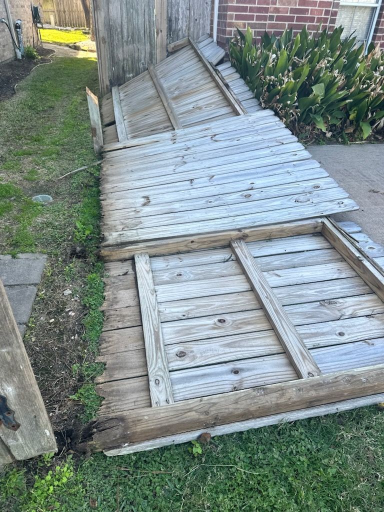 Fallen wooden fence panels on grassy ground next to a brick building.