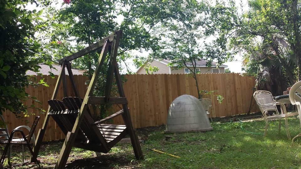 Wooden swing set in a grassy backyard with a wooden fence and trees.