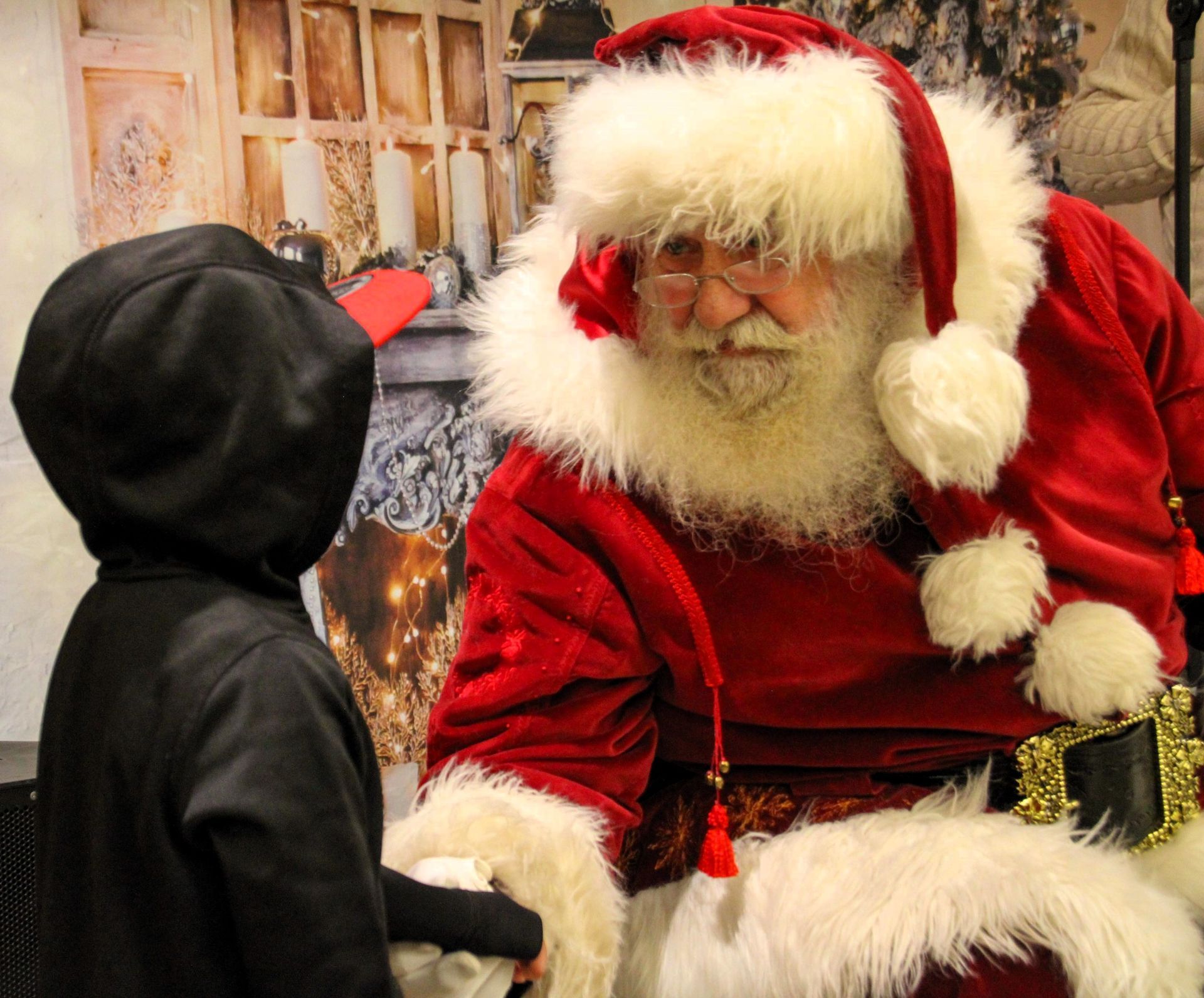 A child in a black hoodie shakes hands with santa claus