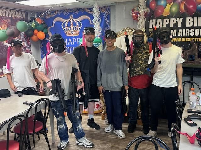 A group of people are standing in a room with balloons and a sign that says happy birthday