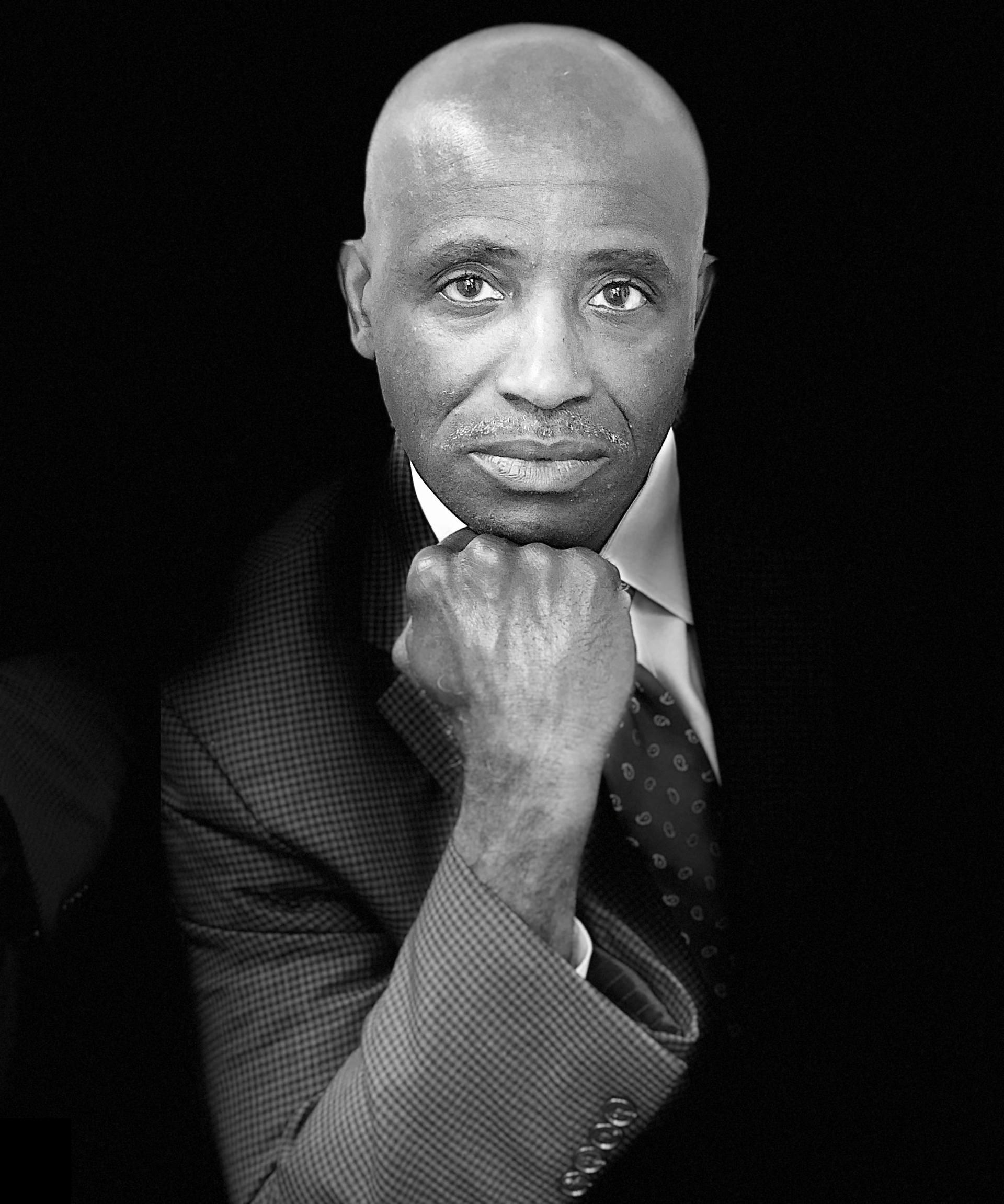 A black and white photo of a man in a suit and tie with his hand on his chin.