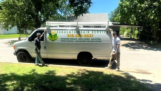 Two men are standing next to a white van that says drain service on it.