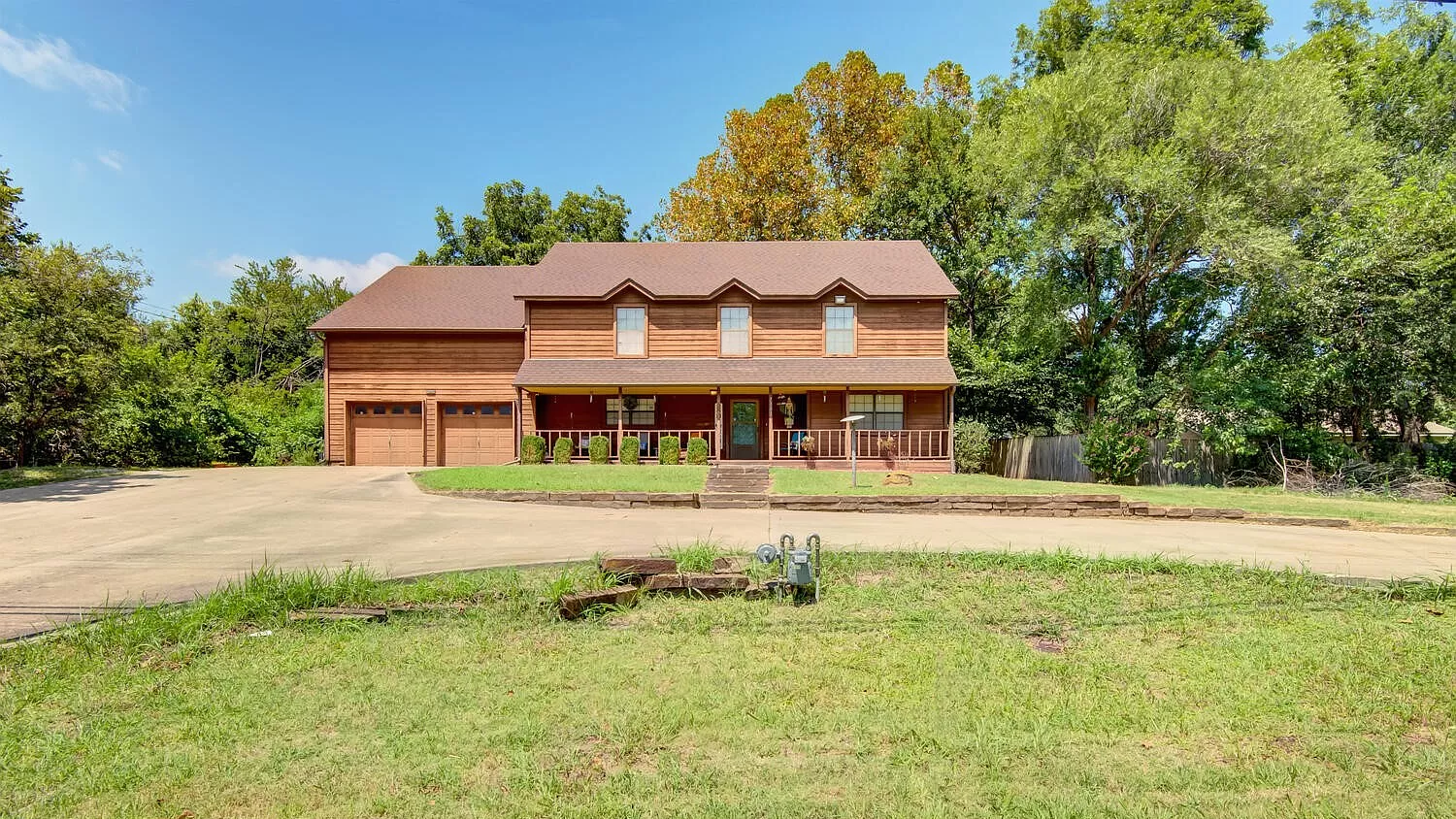 A large log cabin sitting on top of a lush green field surrounded by trees.