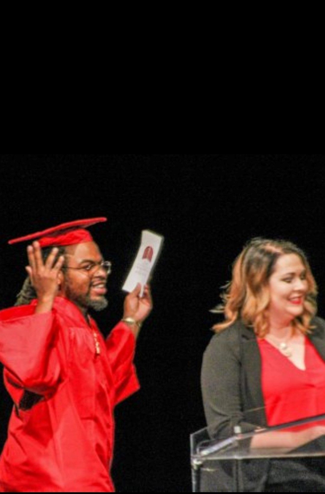 A man in a graduation cap and gown is holding a piece of paper in front of a woman.