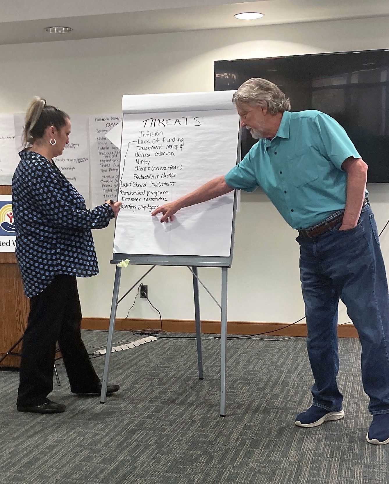 A man and a woman are standing in front of a white board