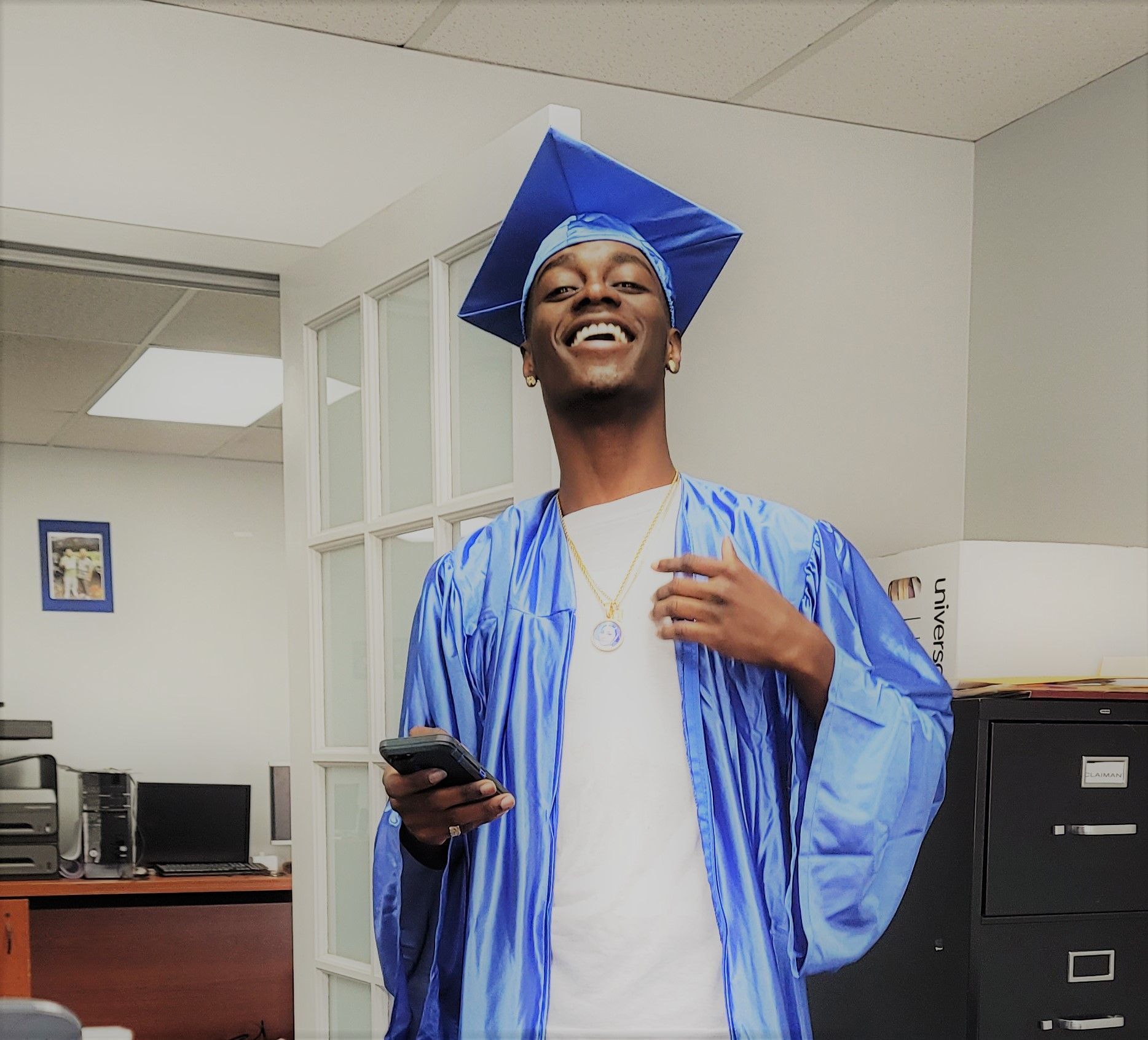 A man wearing a blue cap and gown is holding a cell phone