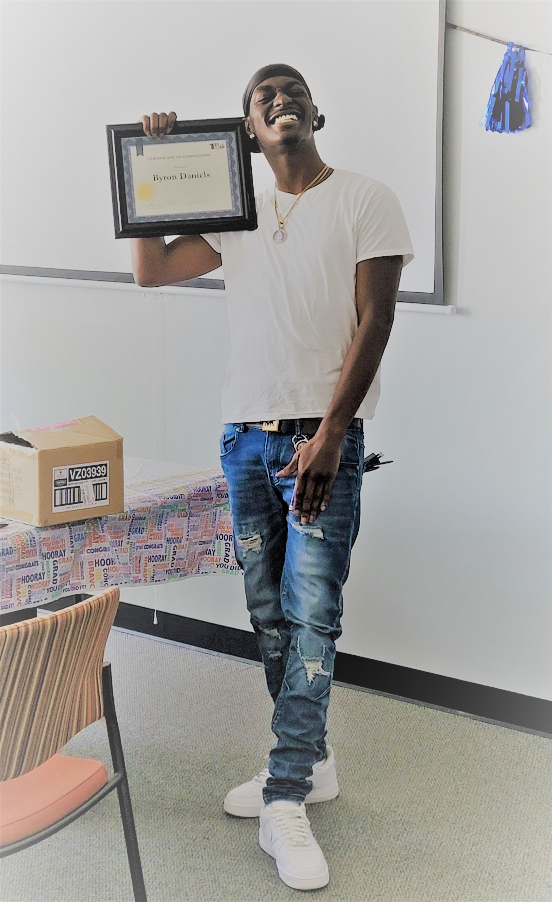 A young man is holding a framed certificate in a classroom.