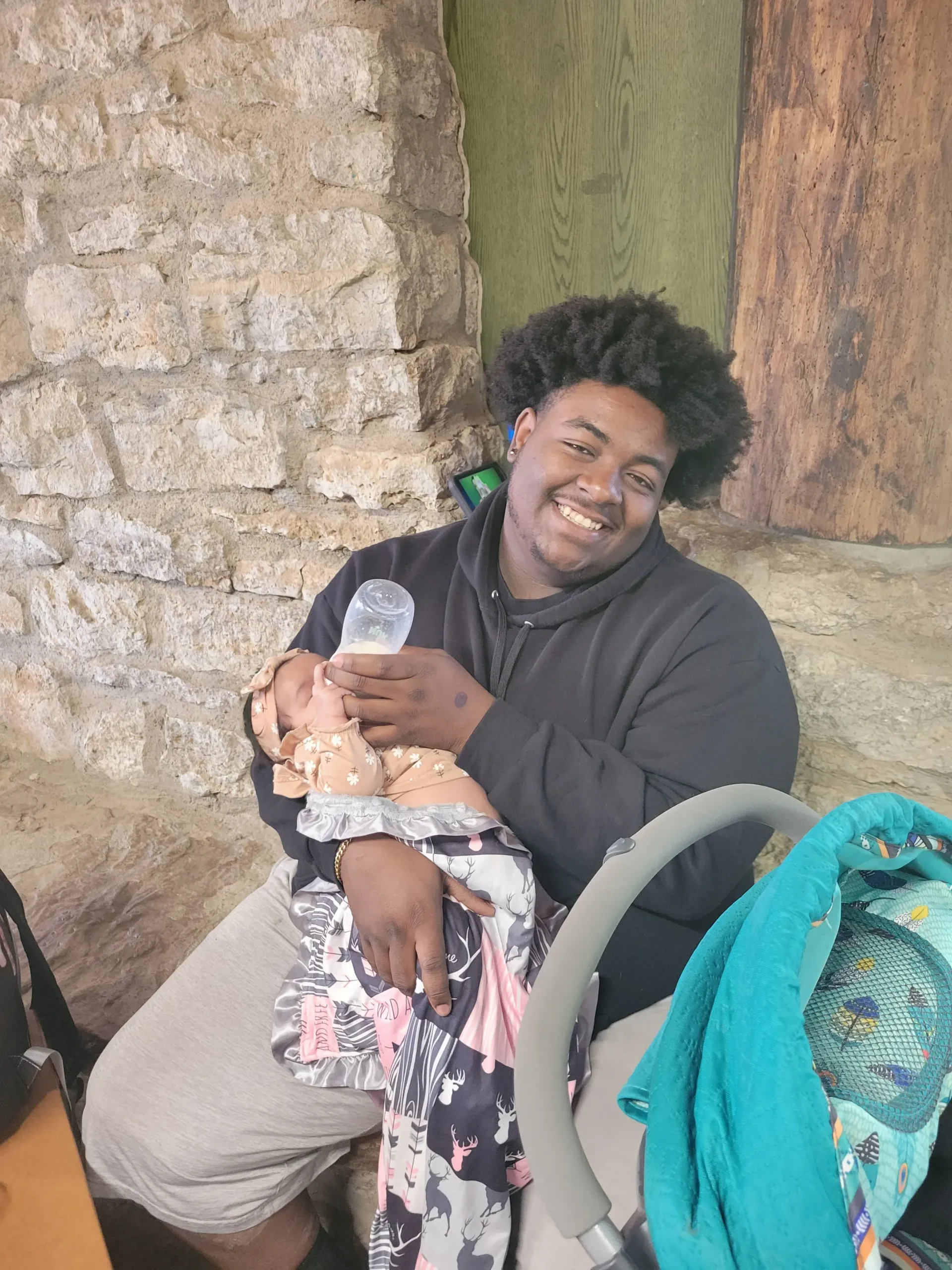 A man is holding a baby and smiling while sitting next to a stroller.