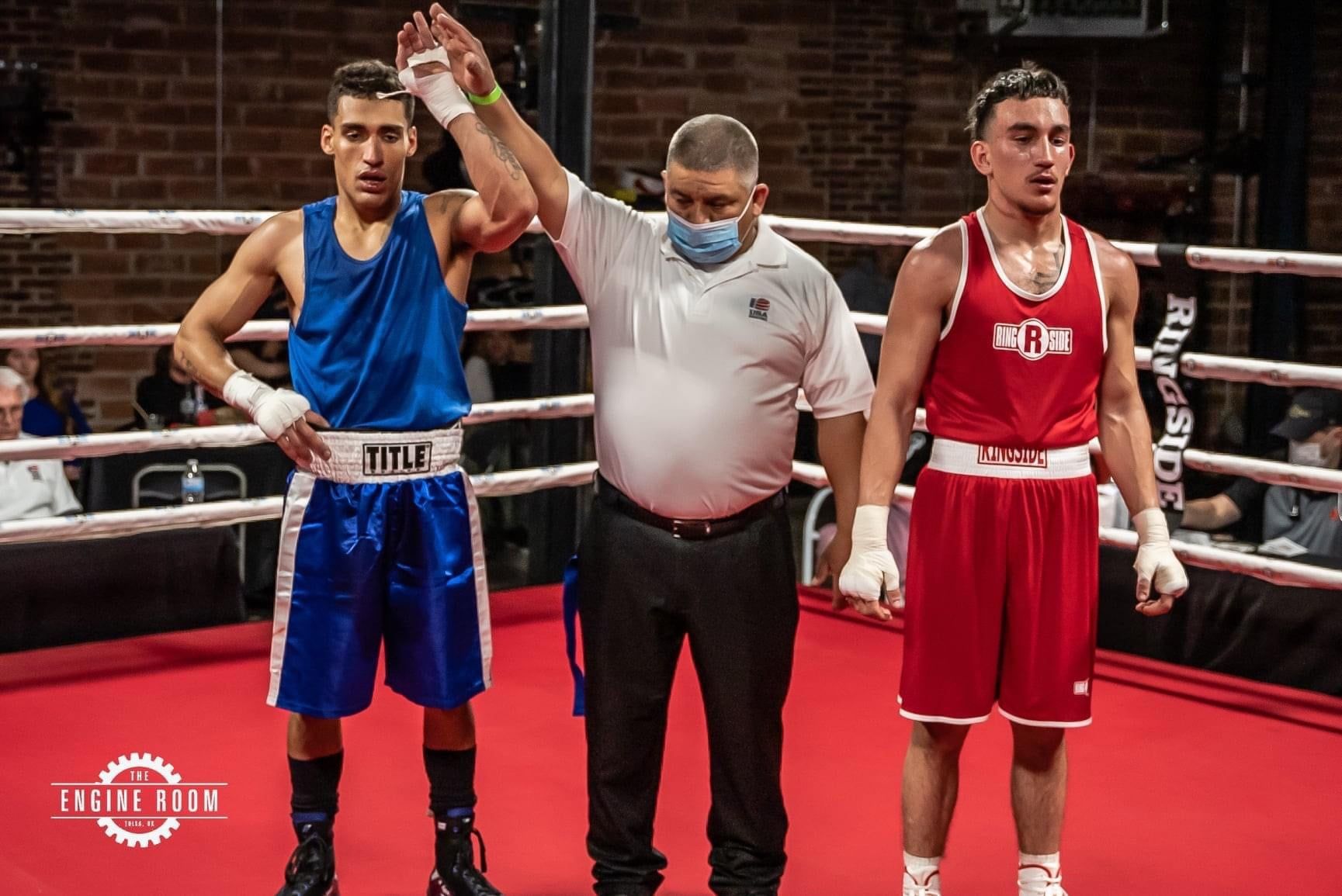 Two boxers are standing in a boxing ring with a referee.