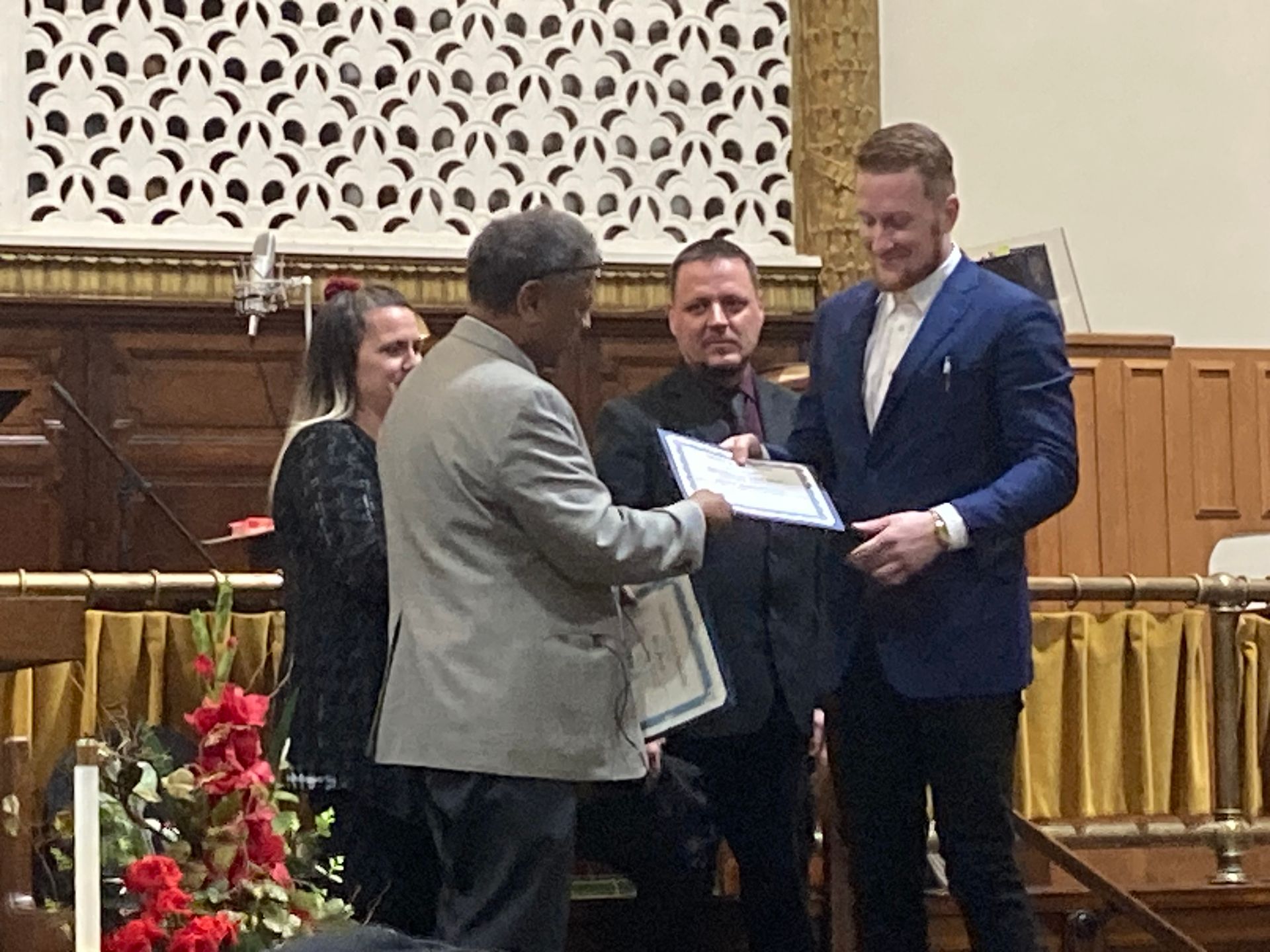 A man in a blue suit is giving a certificate to another man.