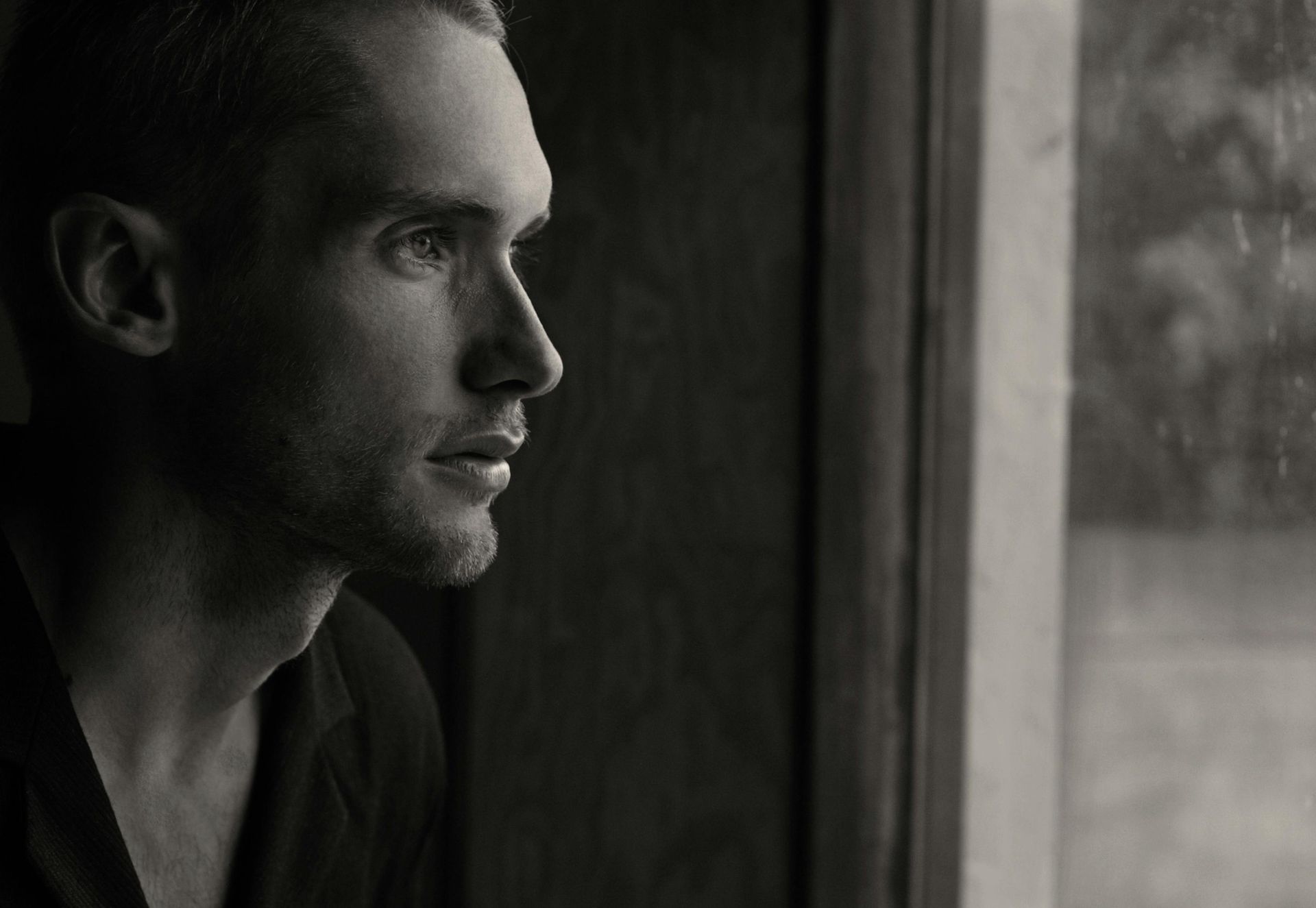 A man is looking out of a window in a black and white photo.