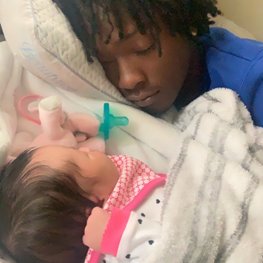 A man is sleeping next to a baby in a bed.