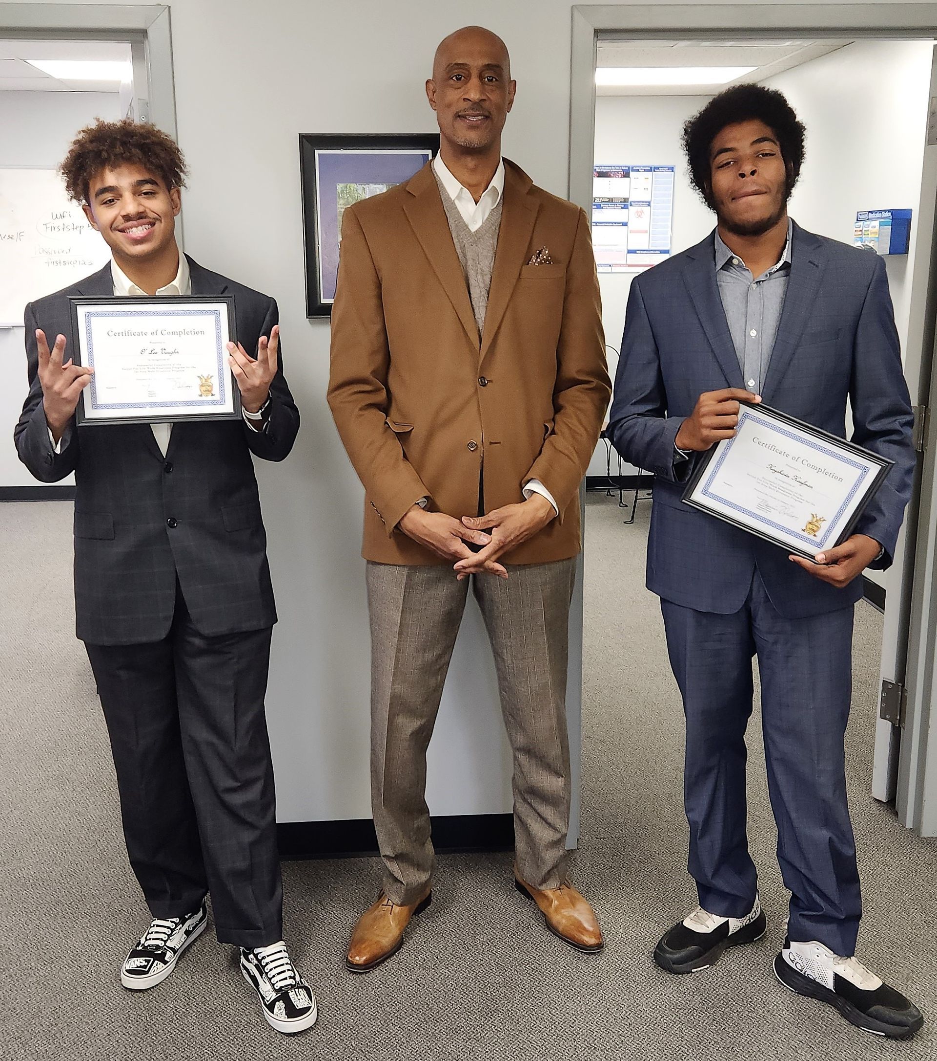 Three men in suits are standing next to each other holding certificates