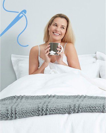 woman in bed smiling and holding a mug