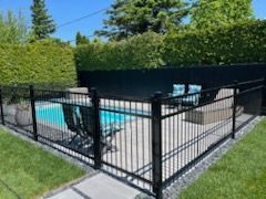 Une clôture noire entoure une piscine dans une cour.