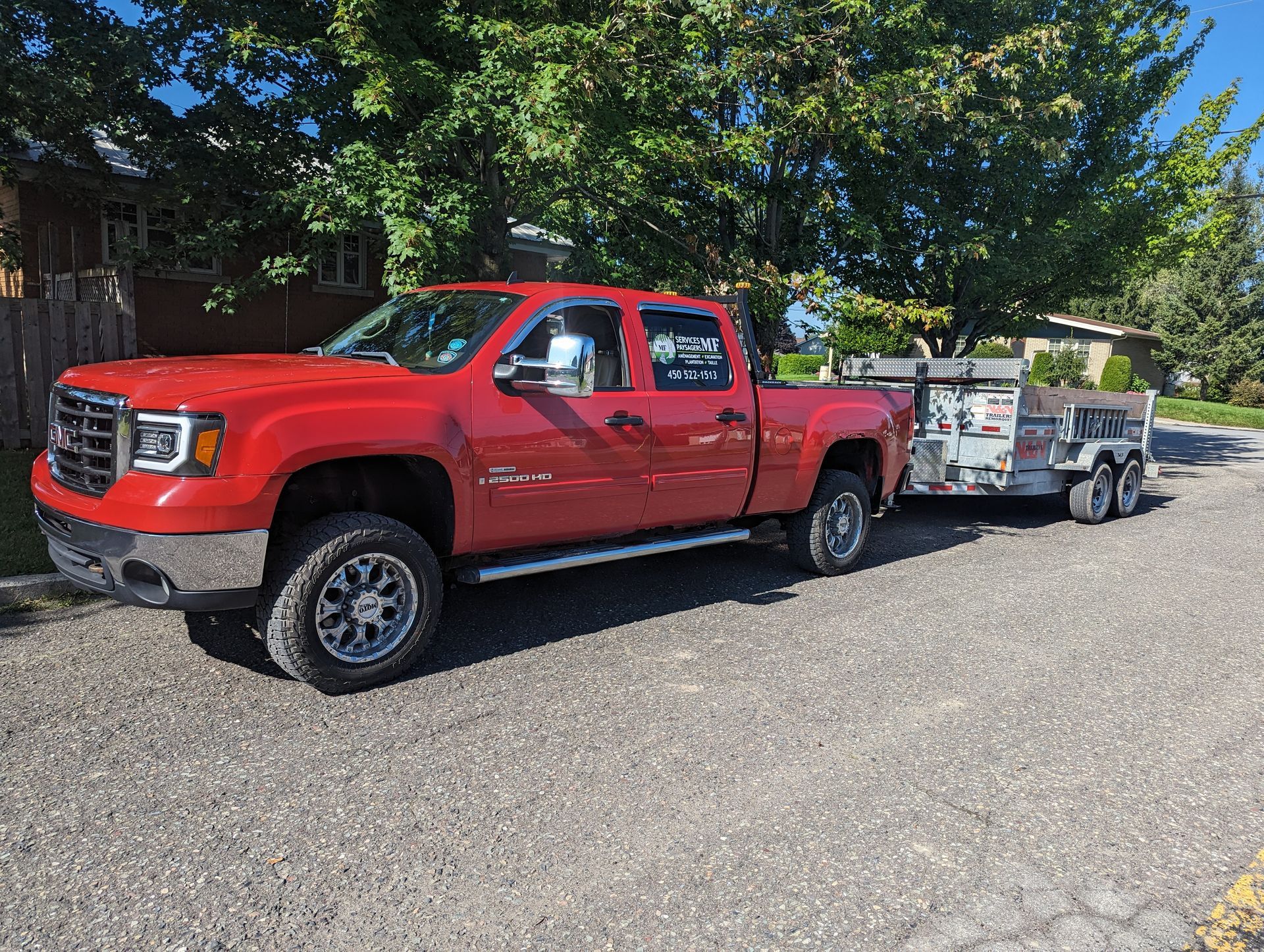 Un camion rouge avec une remorque attachée est garé sur le bord de la route.