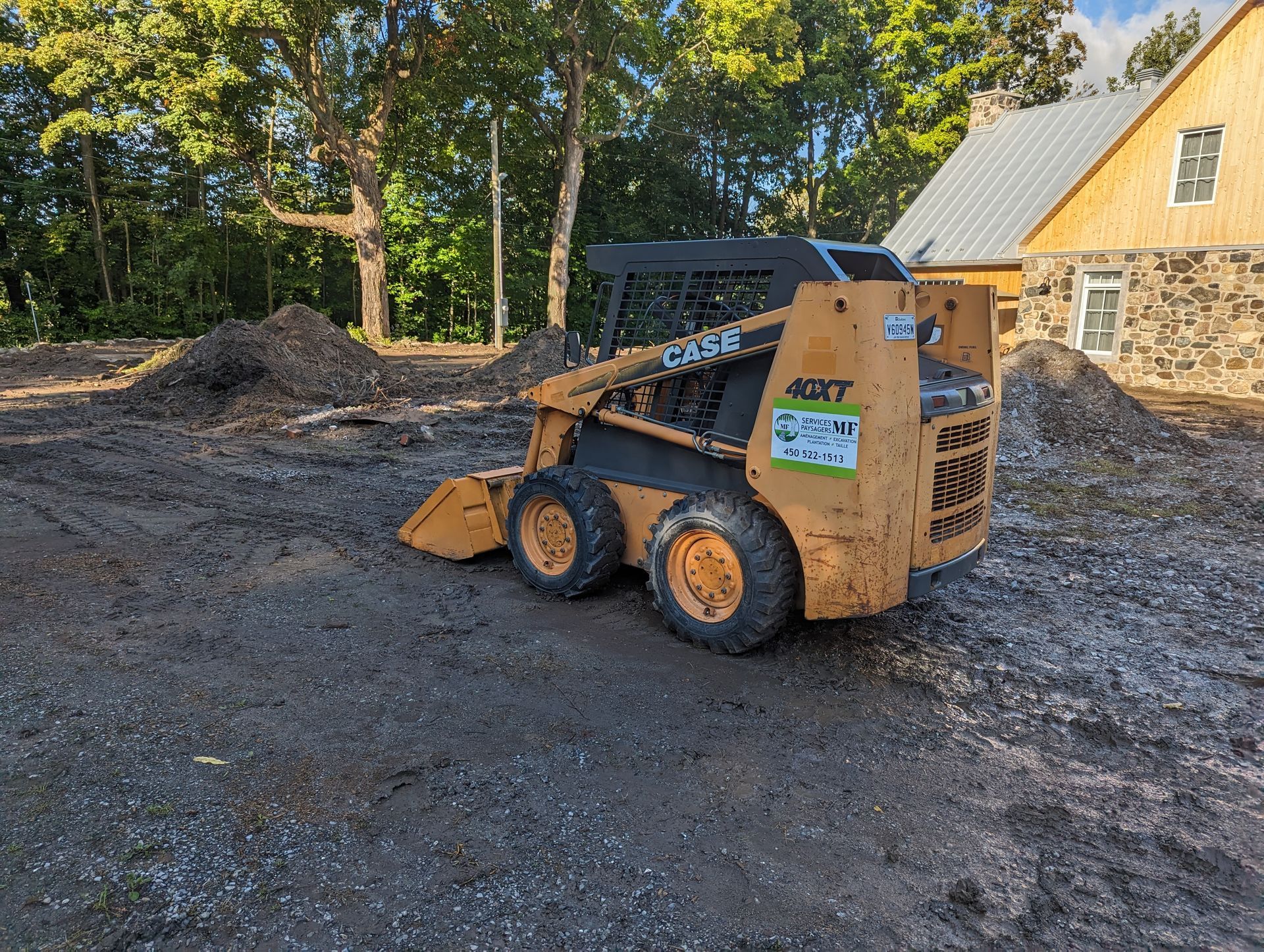 Un petit bulldozer est garé dans un terrain sale devant une maison.