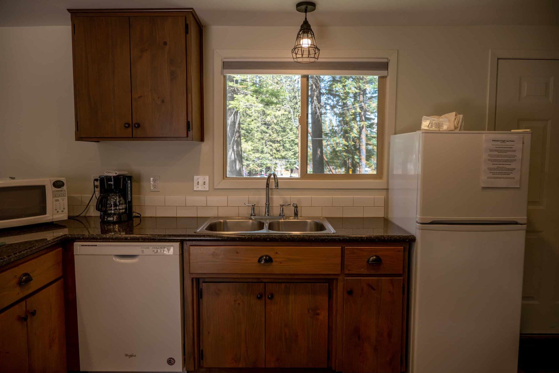 A kitchen with a sink , refrigerator , dishwasher , microwave and window.