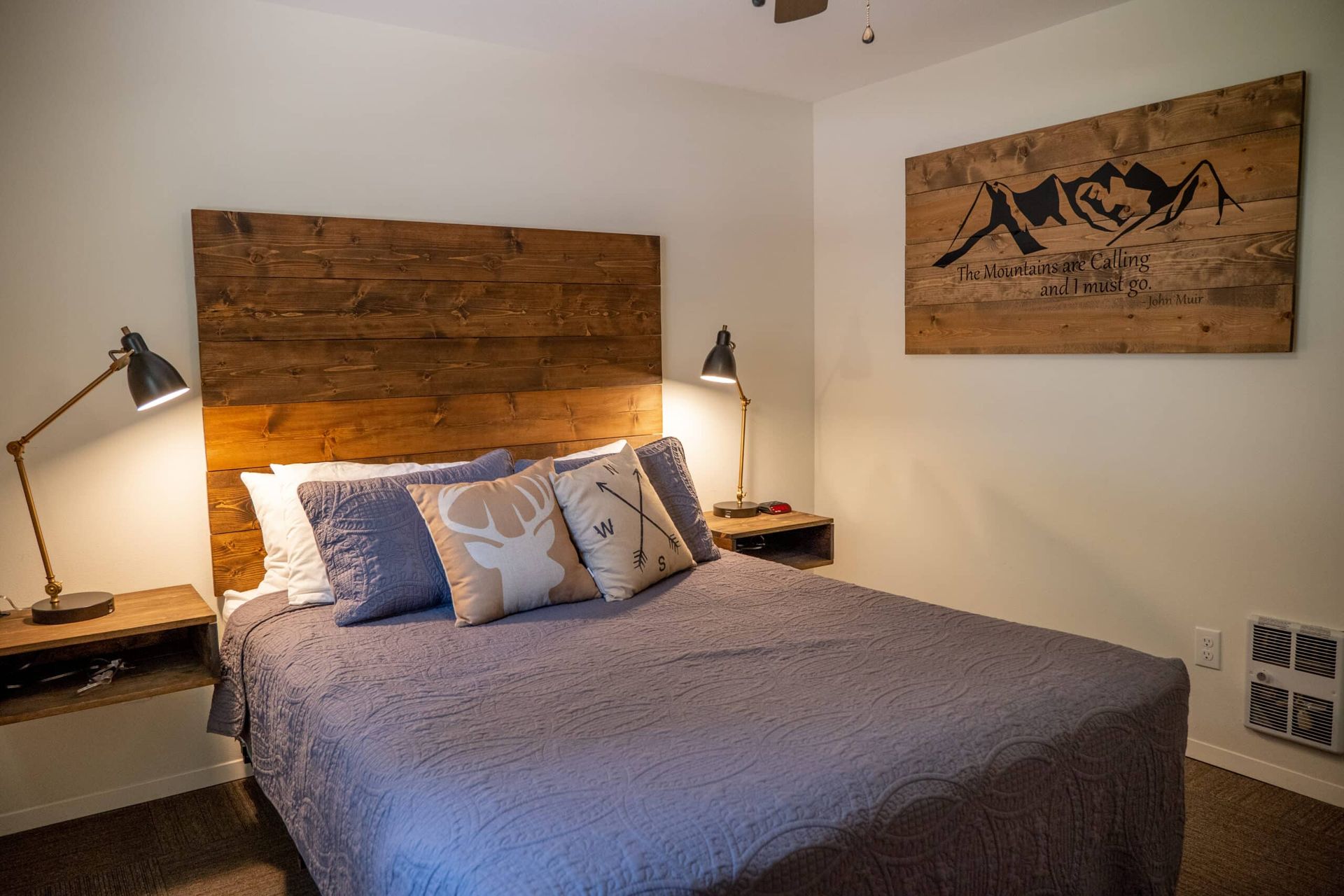 A bedroom with a bed , nightstands , lamps and a wooden headboard.