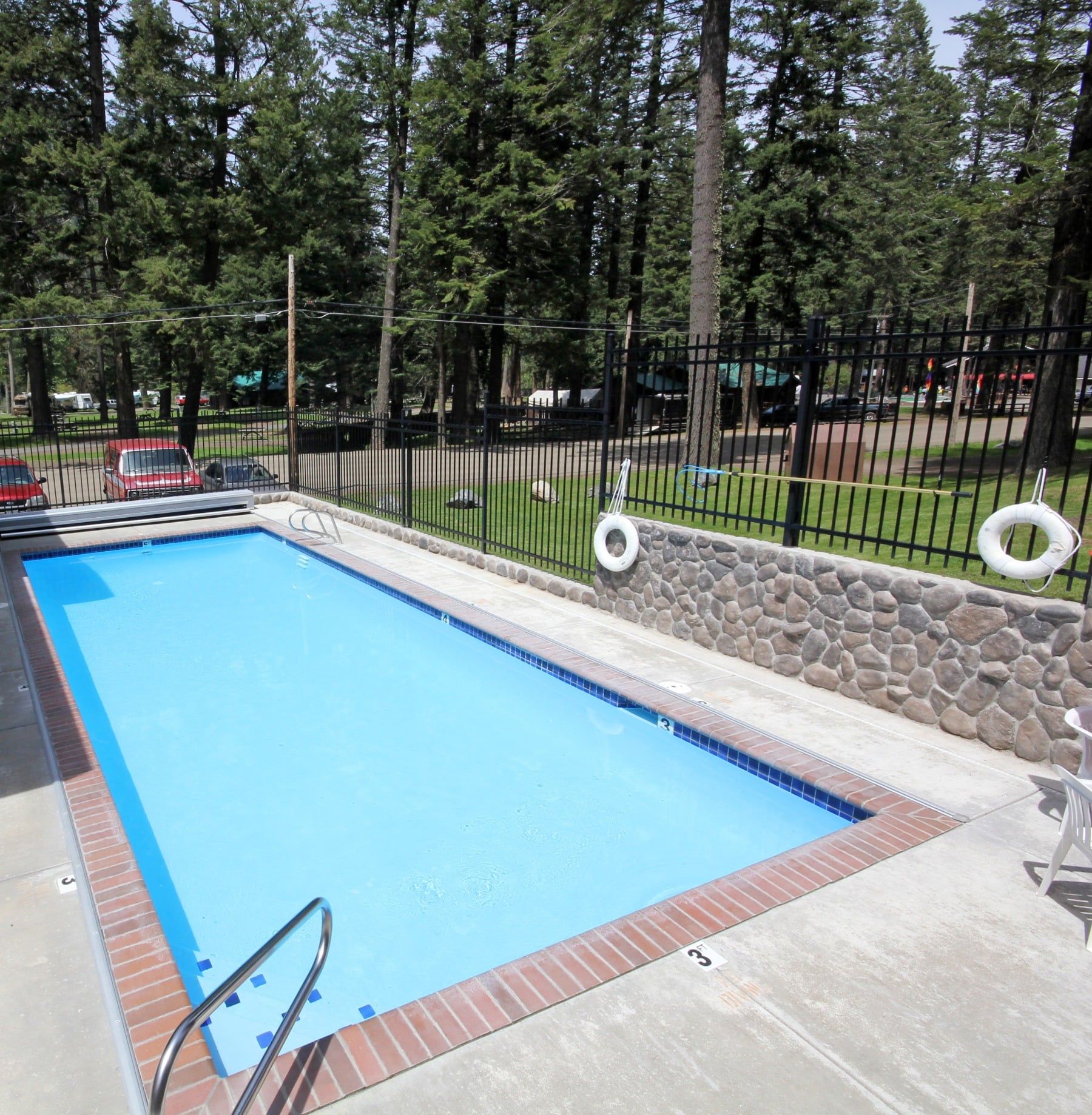 A large swimming pool surrounded by trees and a stone wall