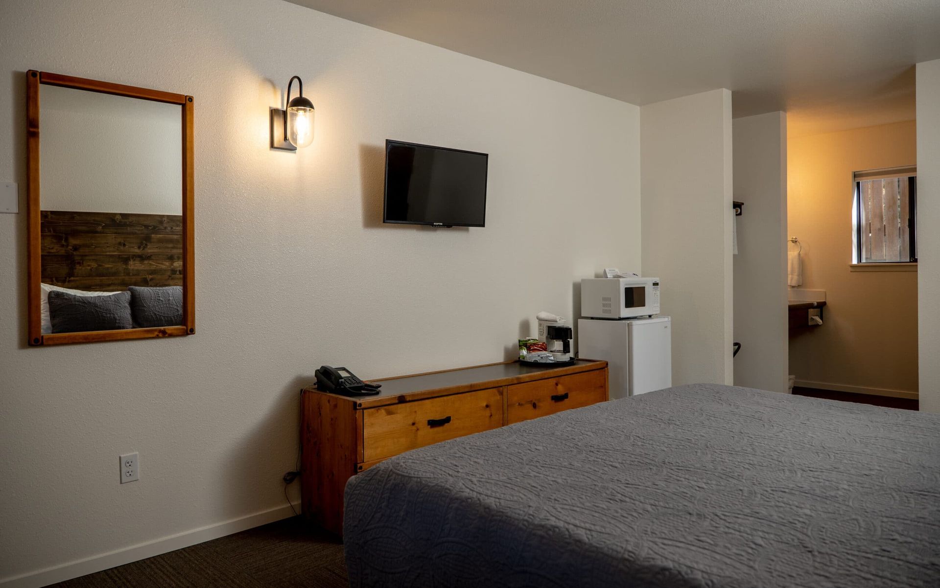 A hotel room with a bed , dresser , microwave and television.