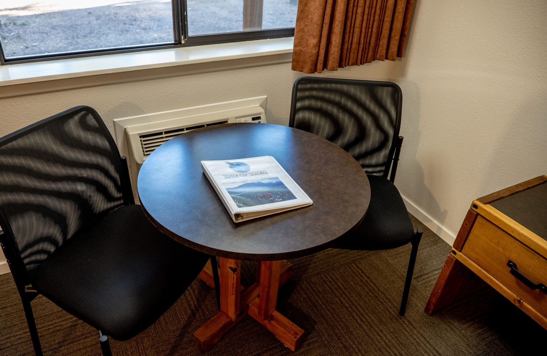 A small table with two chairs and a book on it in a hotel room.