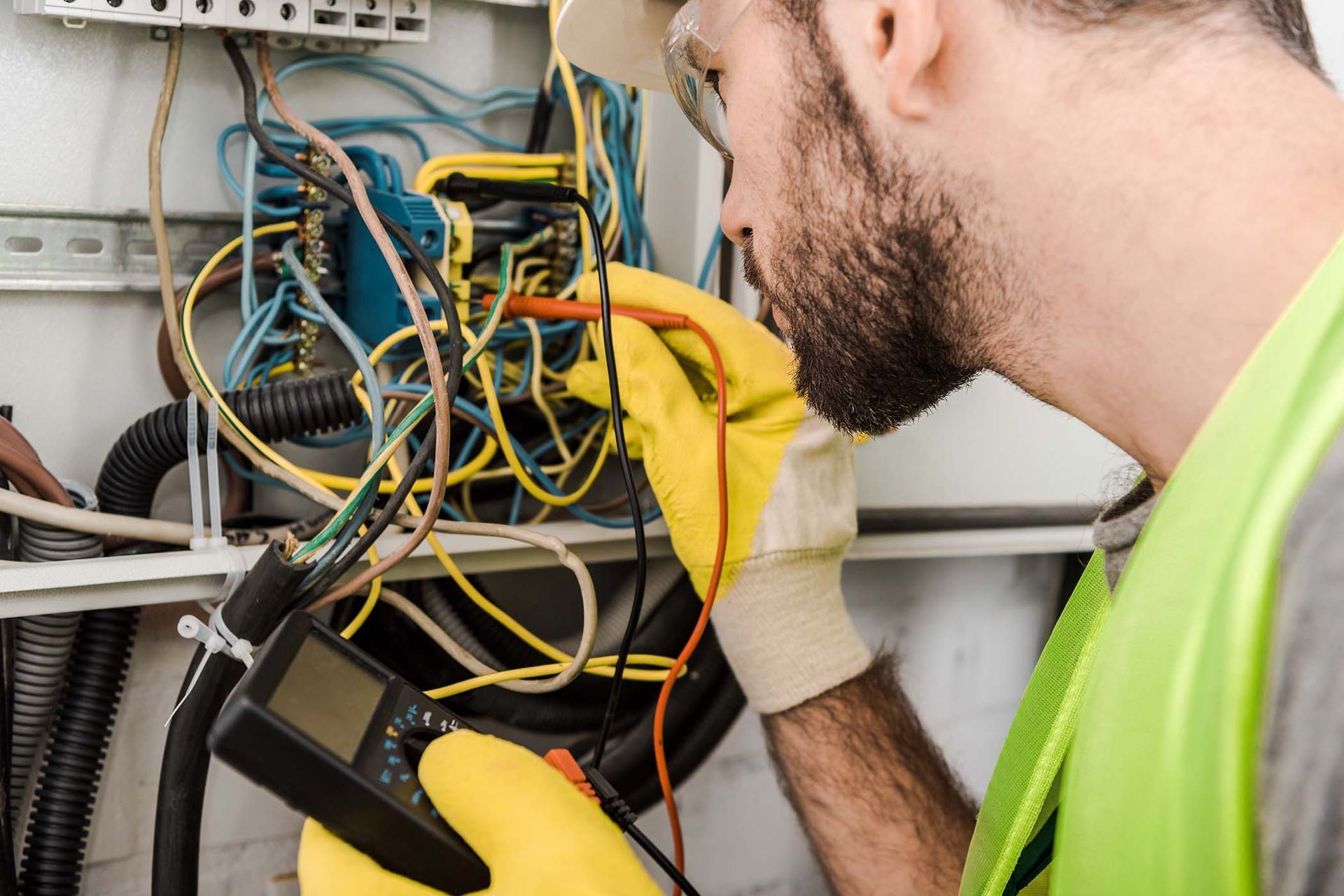 An electrician is working on an electrical box with a multimeter.