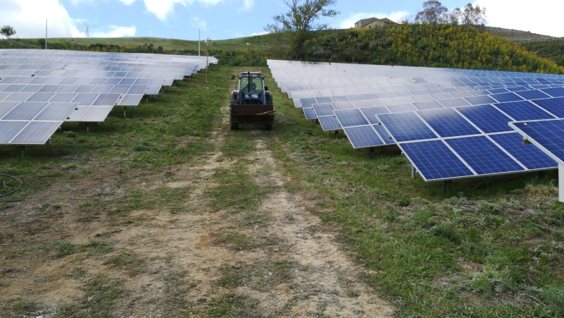 Un trattore sta attraversando un campo di pannelli solari.