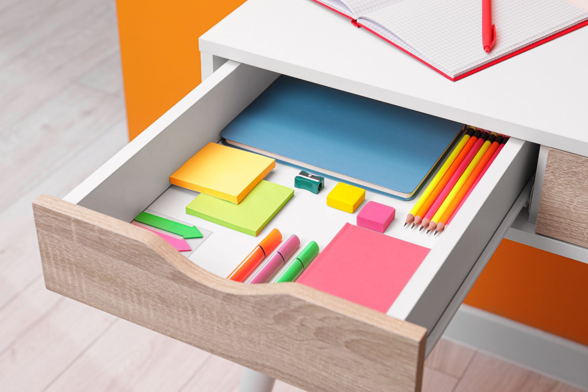 A drawer filled with school supplies on a desk.