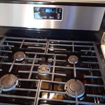 Stainless steel gas stove with five burners and a digital oven control panel.