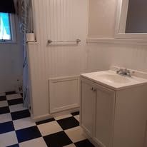 Small bathroom with black-and-white checkered floor, white vanity, towel bar, and doorway to shower area