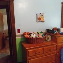 Wooden dresser with a basket of stuffed animals in a room with a white wall and green trim