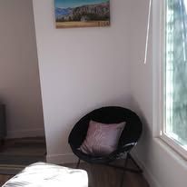 Corner of a bright room with a black chair, pink cushion, window, and small wall art.