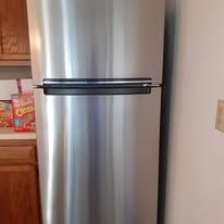 Stainless steel refrigerator in a kitchen, with wood cabinets visible at left.