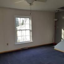 Empty room with blue carpet, white walls, and a window with blinds and daylight.