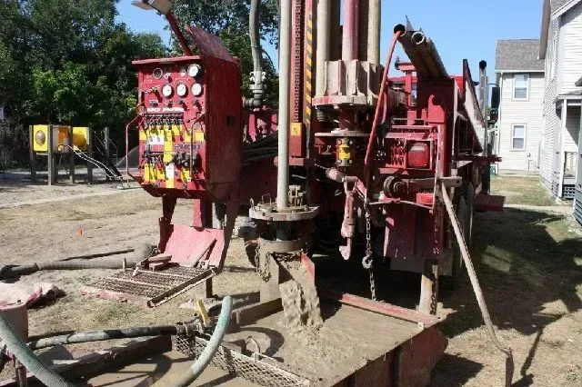 A large red machine is sitting in the dirt in front of a house.