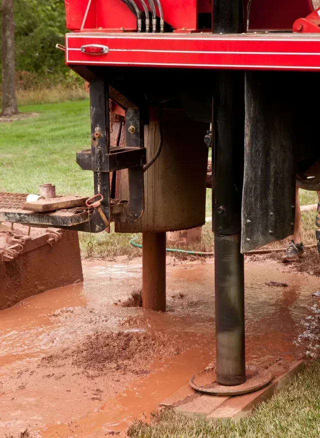 A drilling rig in a muddy field, red machinery, drilling a well.