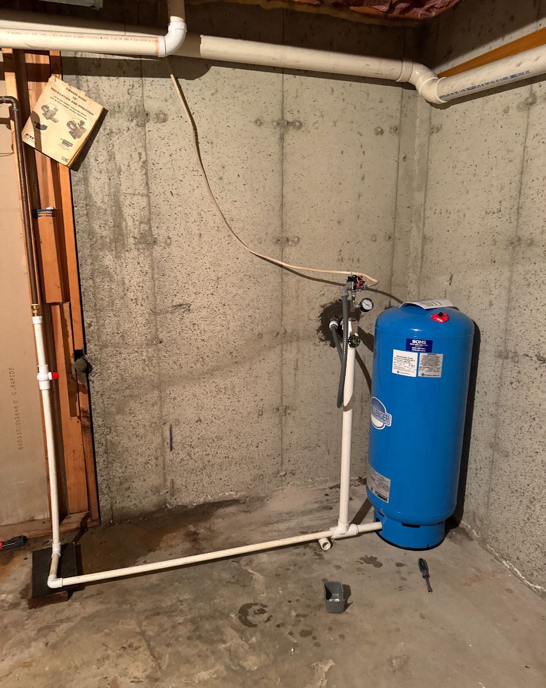 Blue water tank and pipes against a concrete basement wall.