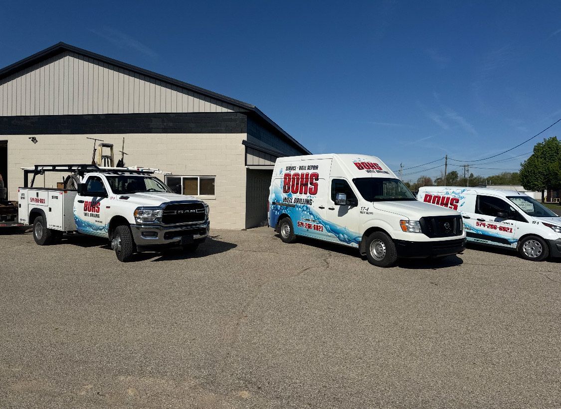 Three white service vehicles parked in front of a tan building under a blue sky.