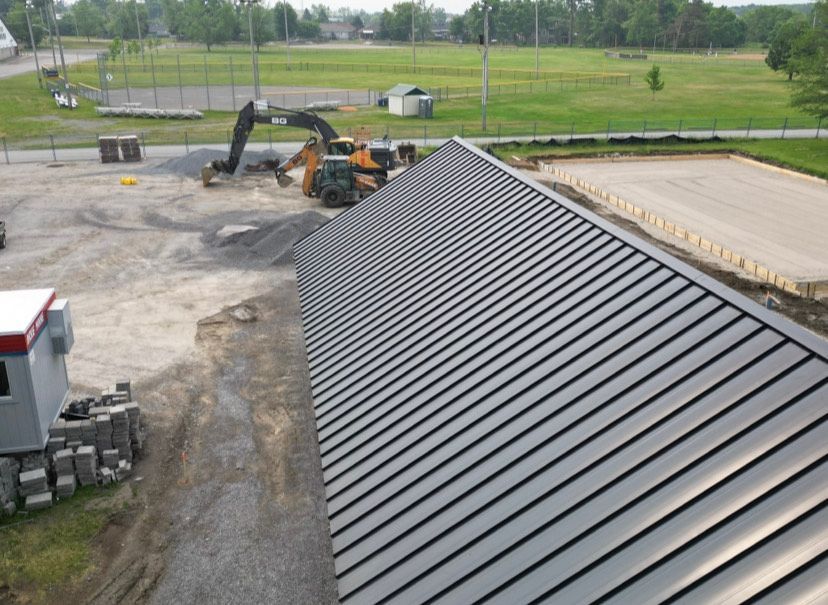 Metal roof over a building; construction equipment and gravel yard in the foreground.