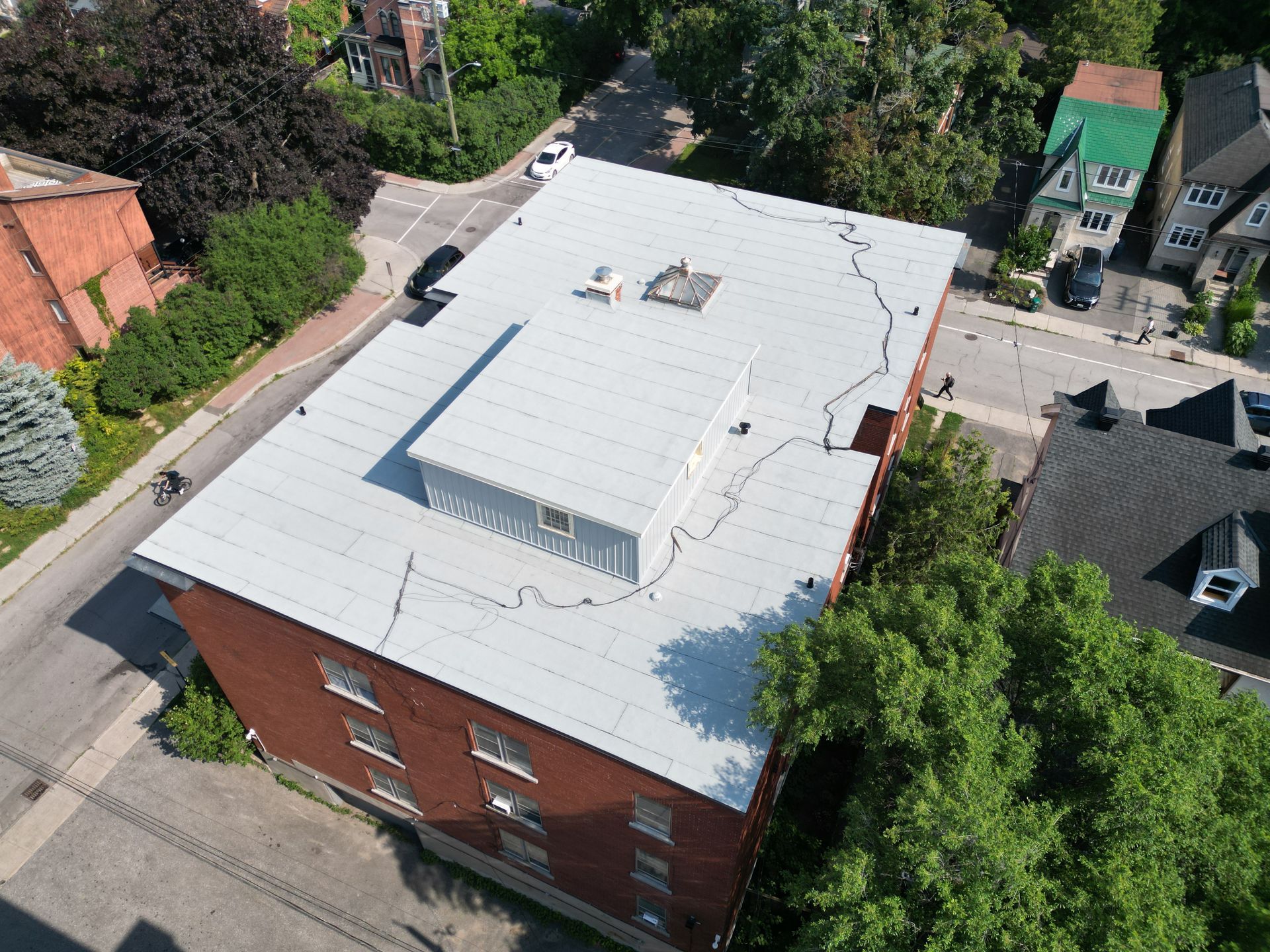 Black roofing membrane being rolled out on a flat roof with snowy background of houses.